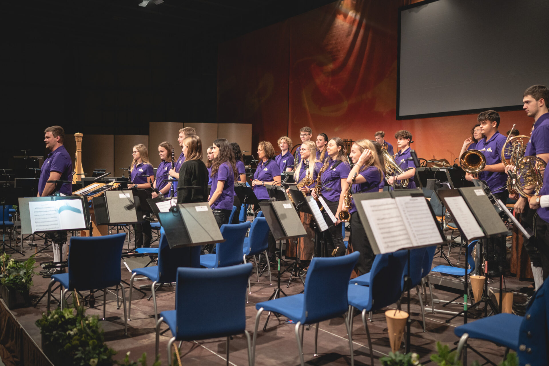 Eine Blasorchester der Stadtkapelle Leonding bereitet sich auf der Bühne auf einen Auftritt vor, wobei Musiker verschiedene Blas- und Schlaginstrumente in der Hand halten.