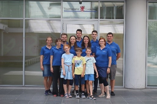 Eine Gruppe von Personen in passenden blauen Hemden posiert für ein Foto vor dem Gebäude der Stadtkapelle Leonding.